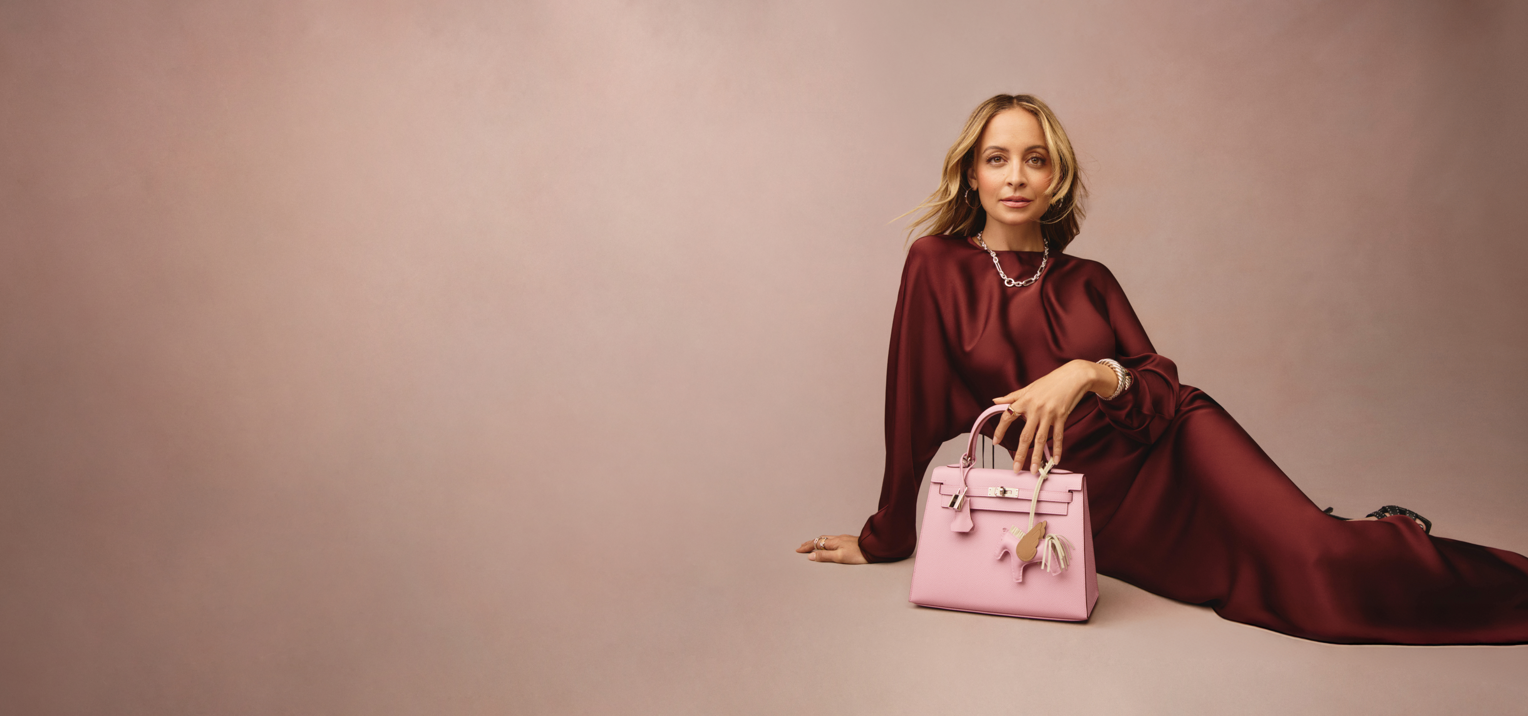 Nicole Richie wearing a burgundy satin long sleeve maxi dress and holding a light pink Hermes Kelly bag