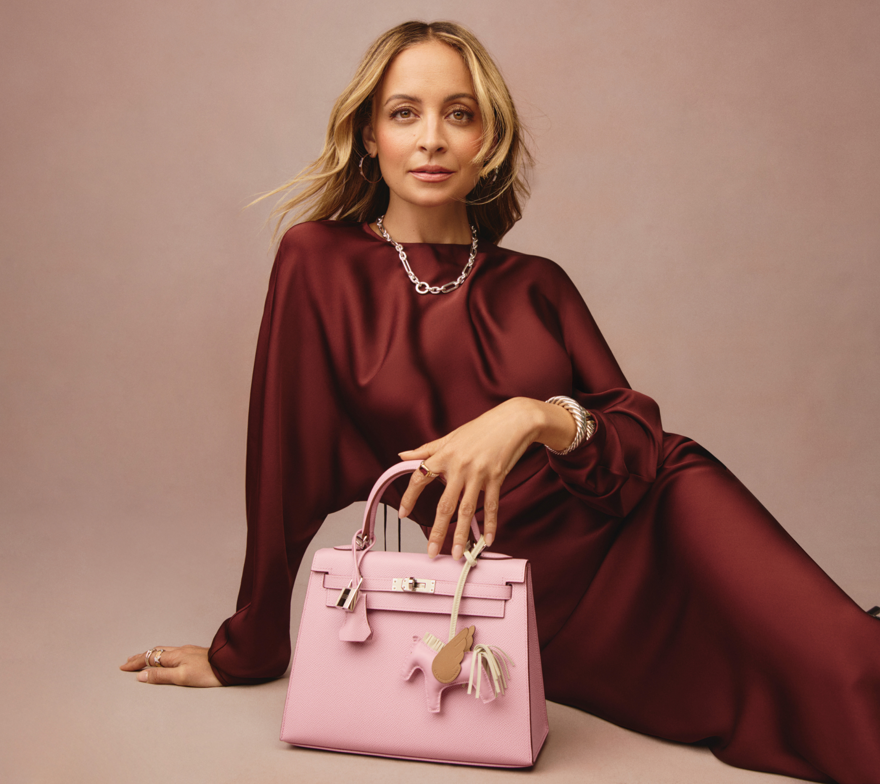 Nicole Richie wearing a burgundy satin long sleeve maxi dress and holding a light pink Hermes Kelly bag