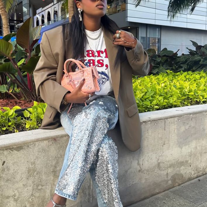 A woman in jeans and an olive green blazer holding a pink Balenciaga Mini City Bag